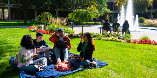 Students sit on a blanket and talk by the fountain.
