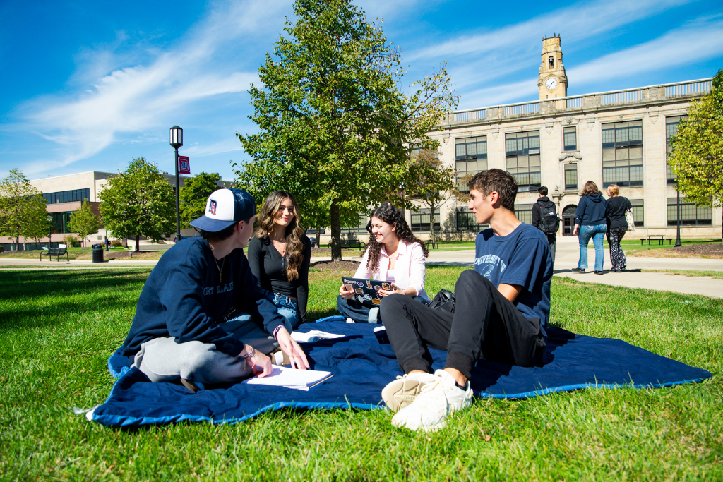 Students sit on a blanket on campus.